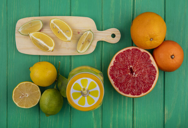 一半俯视图：绿色背景上的切菜板上放着柠檬 橙子和半个葡萄柚的酸橙片柠檬切木板