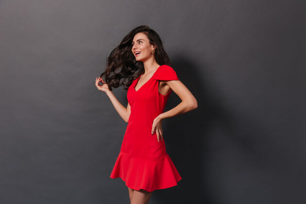 红色连衣裙美丽的女人 华丽的卷发 在黑暗的背景下摆出红色的姿势点套头衫肖像
