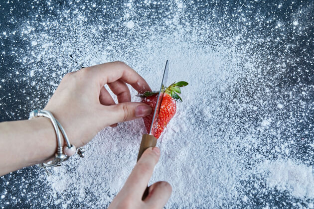 草莓用刀在蓝色表面切新鲜草莓的女人手成熟粉