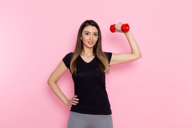 运动正面图年轻女性手持浅粉色桌上的红色哑铃运动员运动锻炼健康锻炼轻观点年轻
