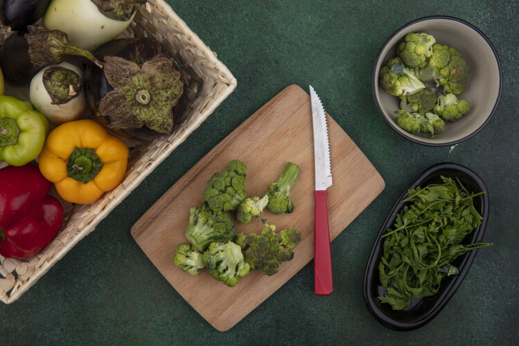 切顶视图甜椒和茄子放在一个篮子里 西兰花放在菜板上 刀子放在绿色的背景上篮子铃铛西兰花