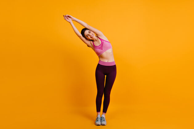减肥黑发女人在黄色的墙上伸展健身交叉健身女孩