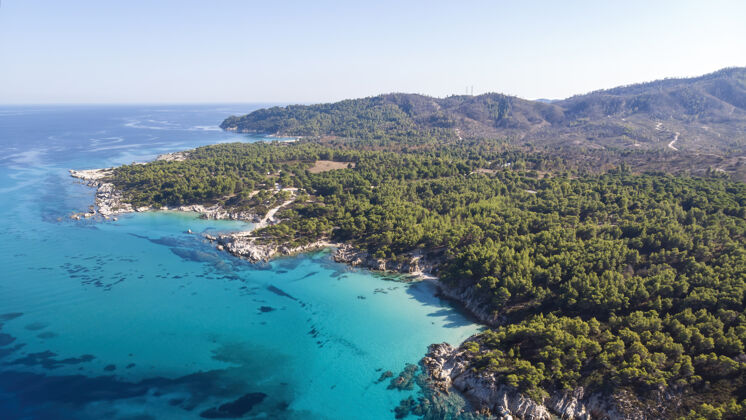 希腊爱琴海沿岸有蓝色透明的海水 周围绿树成荫 岩石 灌木丛和树木 从无人驾驶飞机上俯瞰希腊度假村山海滩
