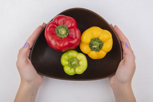 蔬菜俯视图：一个女人拿着彩色甜椒在白色背景的碗里新鲜视图顶部