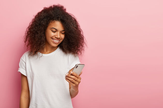 姿势快乐的千禧一代黑人女性 深色卷发 在智能手机上看有趣的视频自由空间高兴女士