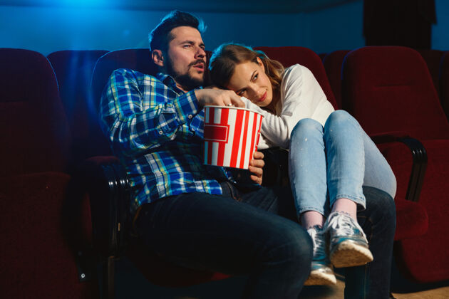 害怕迷人的年轻白种人夫妇在电影院 房子或电影院看电影看起来富于表现力 惊讶和情绪化独自坐着玩关系 爱情 家庭 周末时间吃眼镜微笑