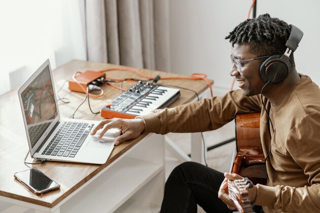 熟练侧视图男音乐家在家里弹吉他和笔记本电脑混合技能男人笔记本电脑
