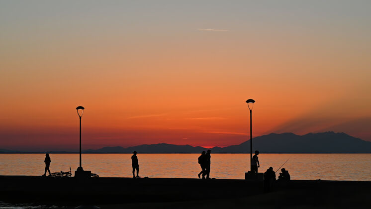 风景码头与多人钓鱼和步行日落时 停放自行车 土地灯柱 希腊地平线暮色日出