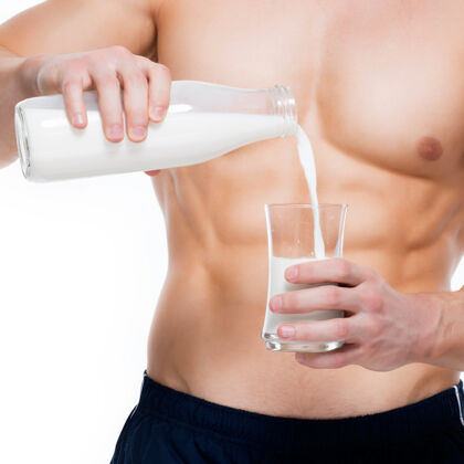 瓶子一个身材完美的年轻人把牛奶倒进一个隔离在白墙上的玻璃里赤膊健美肌肉