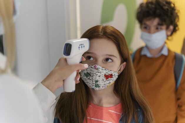 学习老师戴着医用面罩在学校检查孩子们的体温新常态孩子教师