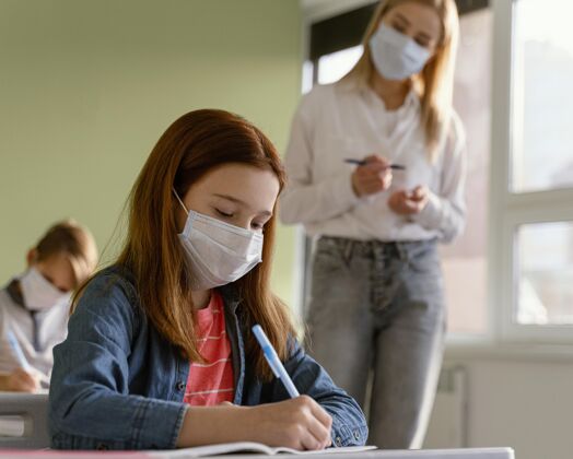 知识戴着医用口罩的孩子在学校和女老师一起学习新常态女性冠状病毒