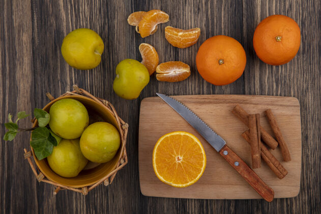甜点俯瞰肉桂与橘子片和刀在砧板上与李子篮子在木制背景食物篮子板