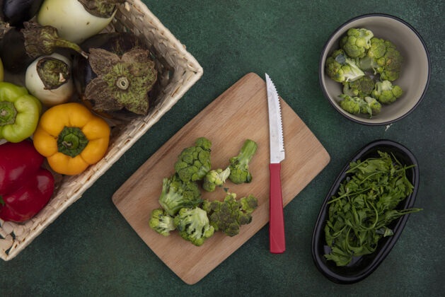 切顶视图甜椒和茄子放在一个篮子里 西兰花放在菜板上 刀子放在绿色的背景上篮子铃铛西兰花