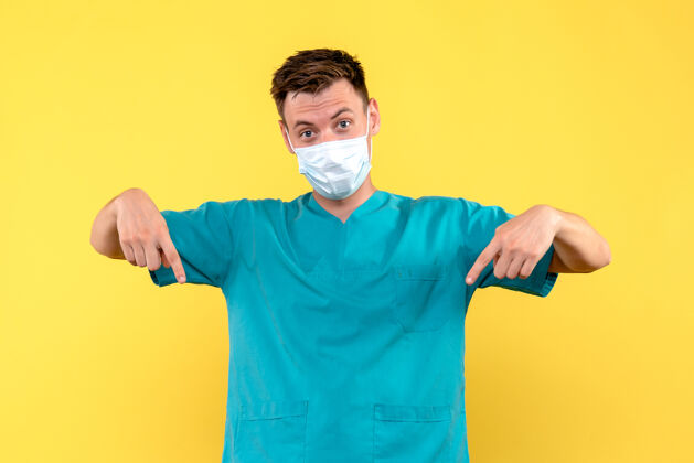 男医生黄色墙上戴着无菌口罩的男医生的正视图男人面具人