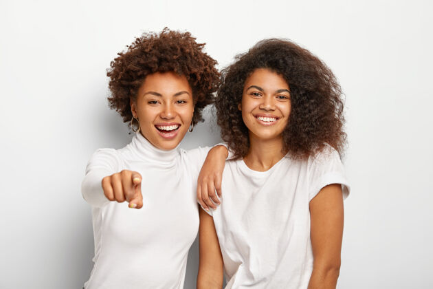 单色快乐友好的两个千禧一代女孩有一张快乐的脸 站在一起 指向远方高兴真诚关系