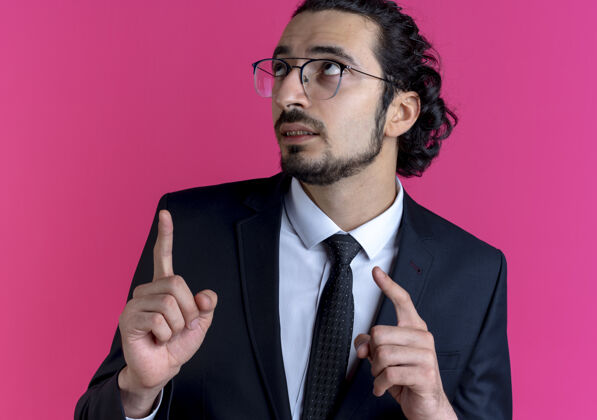 生意人一个穿着黑色西装 戴着眼镜的商人抬起头来 用手指着站在粉色墙上的一边公民领带看
