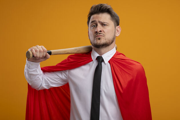 超级英雄身穿红色斗篷的超级英雄商人肩上扛着棒球棒 站在橙色的墙上 看上去很自信站抱商人