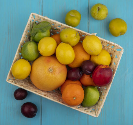 葡萄柚俯视图：将葡萄柚 柠檬 柠檬 橘子 桃子和李子放在一个蓝绿色背景的篮子里酸橙顶部篮子