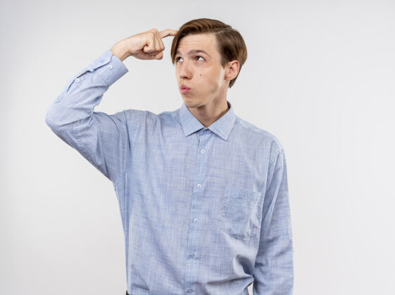 拼图穿蓝色衬衫的年轻人站在白色的墙上 困惑地向一边看 挠头站头靠边