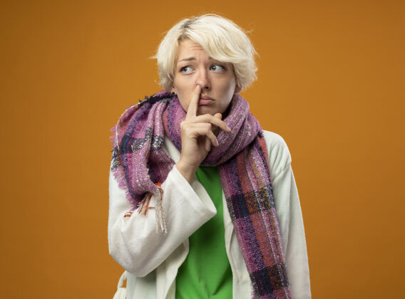 橙色生病的不健康的女人 短头发 戴着暖和的围巾 用手指触摸鼻子 站在橘色的墙上 不开心 悲伤触摸温暖短裤