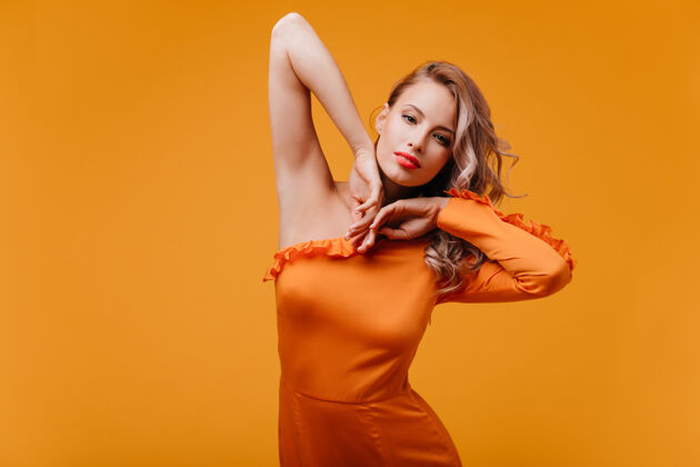 人迷人的苗条女人穿着橙色的裙子在工作室跳舞卷发情感金发
