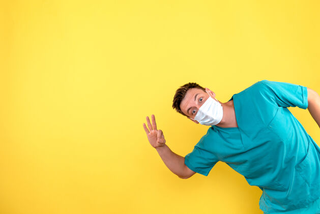 医院黄色墙上戴着无菌口罩的男医生的正视图男性面具人