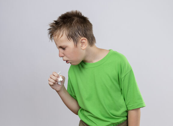 不舒服生病的小男孩穿着绿色t恤 站在白墙上咳嗽 感觉不舒服咳嗽感觉站着