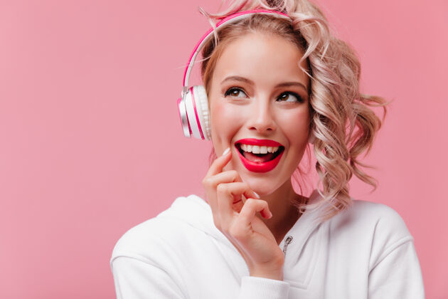 浪漫年轻女子摆姿势 通过她的粉红色耳机听音乐放松服装卷发