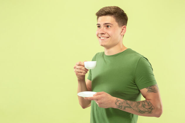 面部以绿色工作室为背景的白人青年半身像穿着衬衫的漂亮男模人类情感的概念 面部表情 销售 广告喜欢喝咖啡或茶手势公司人