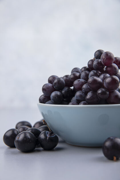 壁板侧视图新鲜的黑葡萄在一个蓝色的碗在一个灰色的背景新鲜黑蓝