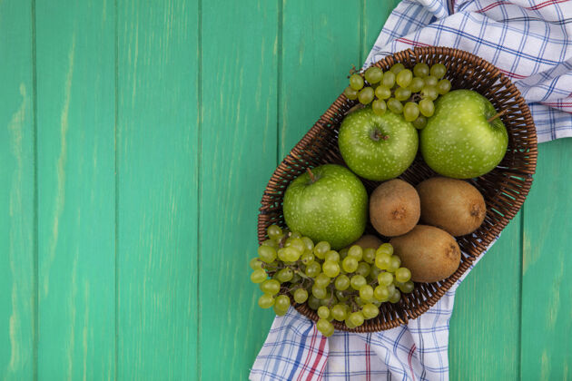 葡萄顶视图复制空间绿色背景上的格子毛巾上的篮子里有猕猴桃和葡萄的绿色苹果毛巾篮子景观