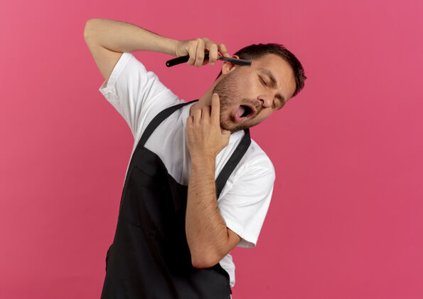 工作穿着围裙的理发师站在粉红色的墙上用剃须刀刮胡子男人T恤市民
