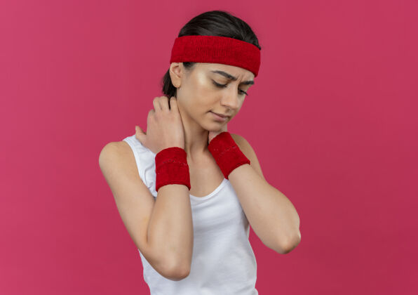 头带穿着运动服的年轻健身女士 头箍贴着脖子 站在粉色的墙上 看上去不舒服 感觉不舒服感觉运动脖子