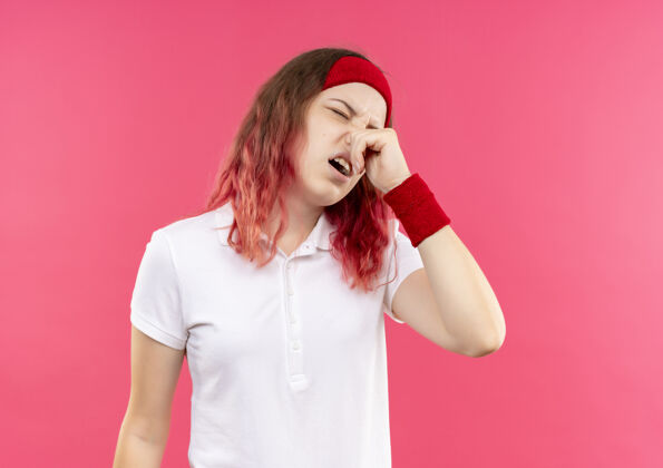 姿势戴着头巾的年轻运动女性站在粉色的墙上 用手指捂住鼻子 忍受着恶臭痛苦女人人