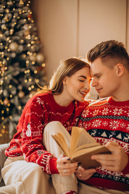 年轻一对夫妇坐在圣诞树旁看书浪漫女朋友礼物