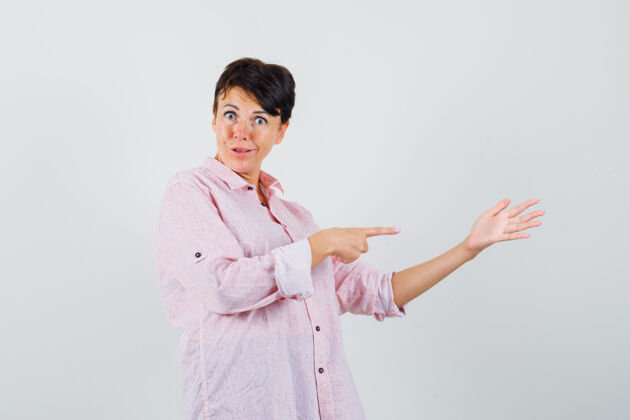 肖像女性指着她摊开的手掌在粉红色的衬衫 看起来困惑 前视图传播指点手掌