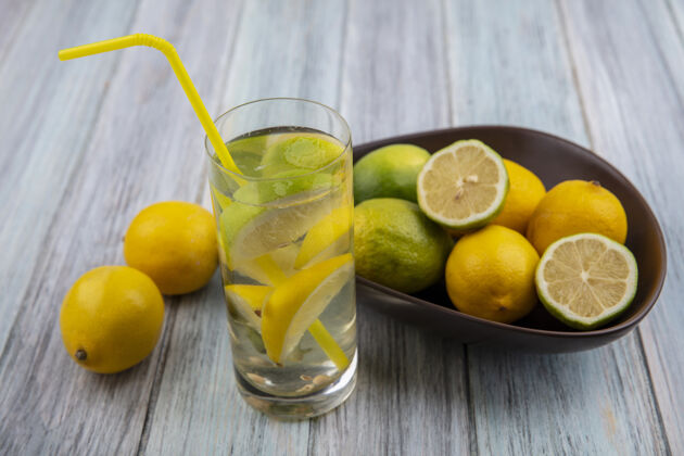 排毒前视图用黄色吸管装在玻璃杯里排毒 灰色背景上用柠檬装在碗里的酸橙视图玻璃柠檬