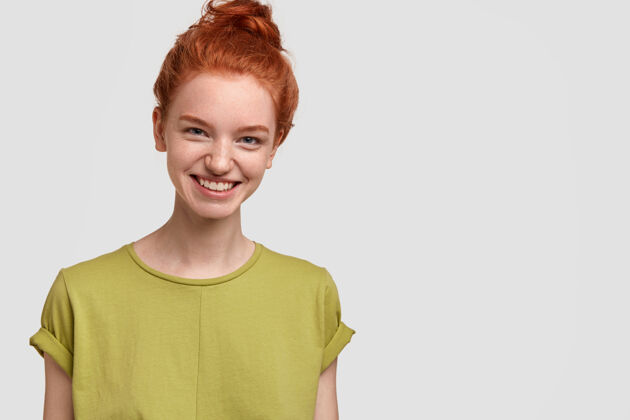 微笑美丽的红发女孩的形象 脸上有迷人的微笑 穿着休闲的绿色t恤 感觉很快乐 隔着白墙 为你的广告内容或促销活动提供了自由空间情感头观点自由空间