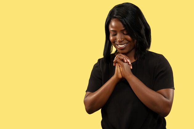专业年轻的非洲裔美国女性 隔离在黄色的工作室背景下 面部表情美丽的女性半身像人类情感的概念 面部表情祈祷和微笑健康年轻非洲裔
