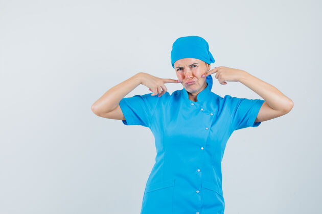 工作人员身着蓝色制服的女医生手指着脸颊 神情悲伤 前视图诊所实验室站立