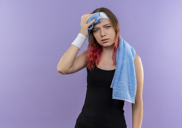 看年轻的健身女孩穿着运动服 脖子上套着毛巾 站在紫色的墙上 看上去又累又累年轻女孩姿势