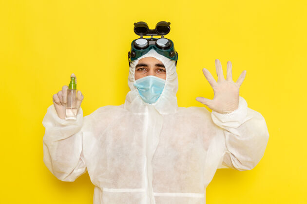 化学正面图穿着特殊防护服的男性科学工作者手持喷雾器在浅黄色的表面持有医生封面