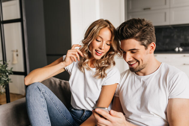 阅读一对幸福的夫妇 带着智能手机看着屏幕 面带微笑两个年轻人在一起享受一天 读着好消息的家庭写真女人欢乐家庭