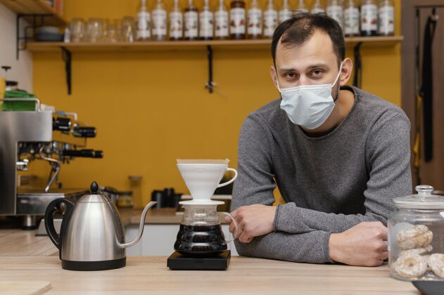 男性前视图中的男咖啡师与医疗面具摆在咖啡店咖啡店职业咖啡馆