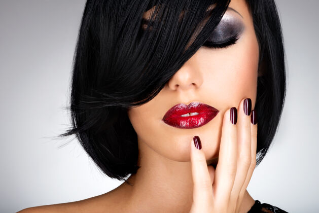 漂亮一张长着漂亮黑指甲和性感红唇的女人的脸一头黑发的时尚模特口红手指直发