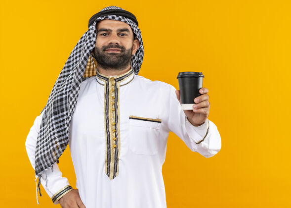 咖啡身着传统服装的阿拉伯商人站在橙色的墙上 脸上露出自信微笑的咖啡杯展示穿着站立