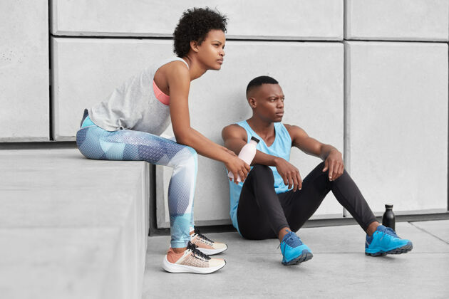 阳刚坚定的男女照片皮肤黝黑 身体健康 有沉思沉思的面部表情 放松的黑人女孩坐在男朋友附近的楼梯上 打篮球后很累运动鞋衣服年轻人