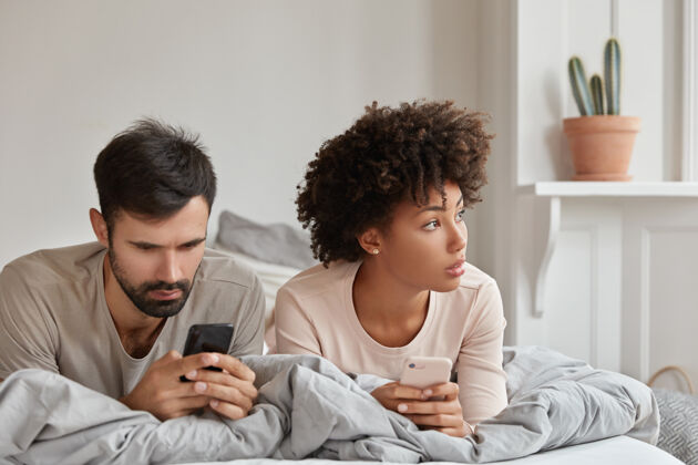 视图图为体贴上瘾的混血男女通过手机应用程序阅读网站 周六上午在床上度过 有技术成瘾夫妇浏览互联网配偶手机家庭