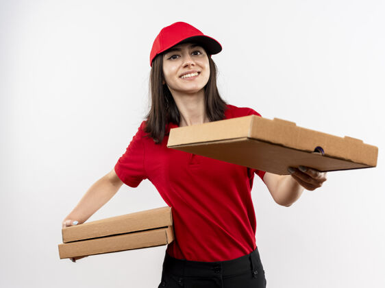 送货身穿红色制服 头戴鸭舌帽的年轻送货员拿着比萨饼盒 站在白色背景上 微笑着向顾客提供其中一个比萨饼女孩披萨提供