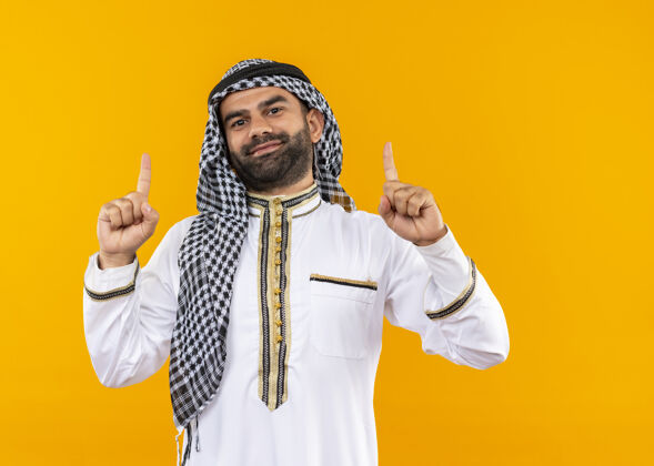 指点身着传统服装的阿拉伯商人用食指指着橙色的墙上 微笑着自信地站着手指商务人士传统